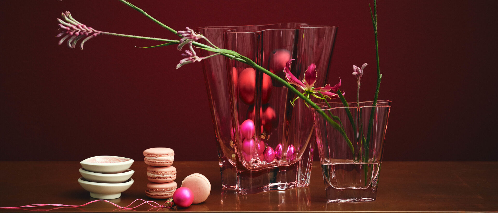Weihnachten 2022 Händlerliste Flux Glasvasen in Rosa mit Blumen und pinken Mini-Weihnachtskugeln gefüllt stehen neben Macarons und Junto Rose Quartz Dipschälchen